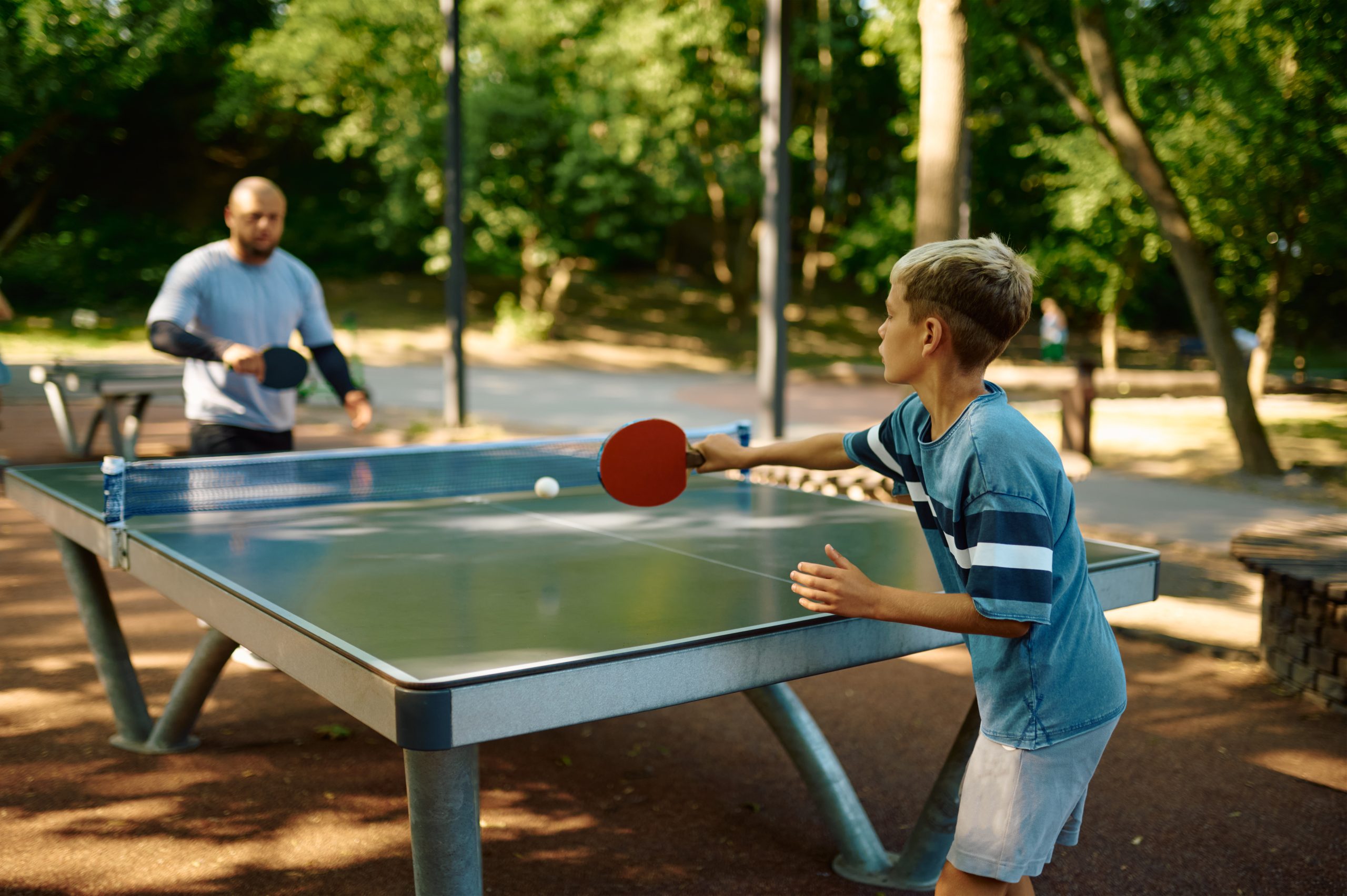Father and son play table tennis outdoors. The family leads a healthy lifestyle, daddy and boy, ping pong training in summer park